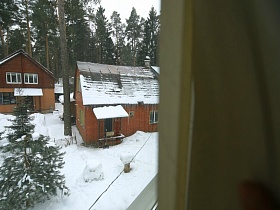 вид из окна второго этажа съемного дома на соседние дома с зелеными елочками на участке в снегу