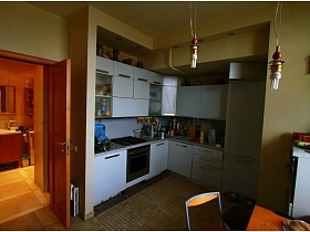 белая кухня с многочисленными шкафами, посудой и электропрборами на светлой столешнице за открытой дверью  зонированной комнаты двушки с видом на Москва-сити