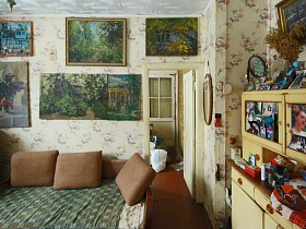 природа на многочисленных картинах художника на стене светлой столовой с мягким диваном и подушками на советской профессорской даче с овальной террасой