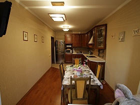 общий вид светлой кухни с коричневой мебельной стенкой, обеденным столом со стульями из лоджии, совмещенной с кухней современной трехкомнатной квартиры с детской комнатой