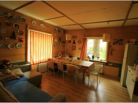 общий вид просторной гостиной с длинным обеденным столом, холодильником, серым угловым мягким диваном современной двухэтажной дачи для съемок кино