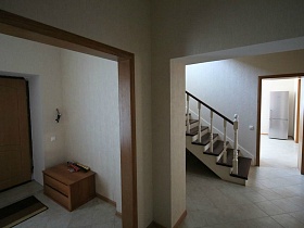 небольшая тумбочка и коврик у входной двери кирпичного дома под съем с лестницей на второй этаж просторного холла