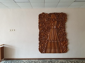 коричневый барельеф с изображением девушки на белой стене лестничной площадки с мозаичным полом в столовой СССР