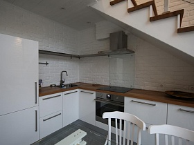 Кухня лофт, кухня под лестницей в квартире лофт, белый шкаф в кухне, белые стулья в лофте, коричневая столешница в лофт квартире