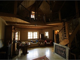 общий вид просторной комнаты отдыха с деревянной лестницей, ведущей на мансарду необычного дома в сосновом лесу