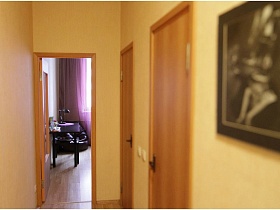 обеденный коричневый стол у стены кухни из открытой двери прихожей с одинаковыми дверьми в ванную и санузел простой квартиры