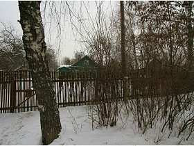 коричневый штакетный забор вокруг зеленой дачи