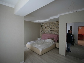 большая кровать с белым постельным у стены с декоративным кирпичом в спальной комнате на этаже таунхауса