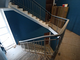 синие стены подъезда жилого дома с редкой винтовой лестницей, большими окнами на лестничной площадке между этажами