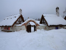 широкие двери в кирпичном заборе с аркой в небольшом дворике ресторана, стилизованного под хутор в коттеджном поселке в зимнее время
