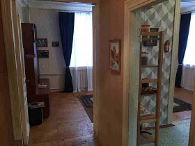 коричневая мебельная горка, фотографии на стене у окна с синими шторами гостиной с двумя выходами в прихожую и кухню кв 27