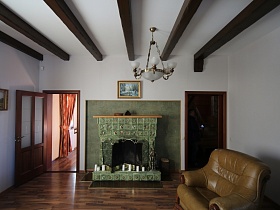 картины на белых стенах гостиной с коричневым мягким диваном и зеленым камином между межкомнатными дверьми загородного дома в сказочном стиле