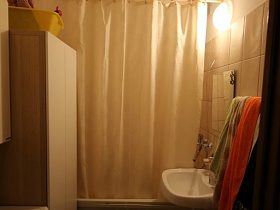 белая ванна с экраном и шторкой, светлый шкаф, стиральная машинка, белая раковина в ванной комнатепросторной современной трехкомнатной квартиры в переезде
