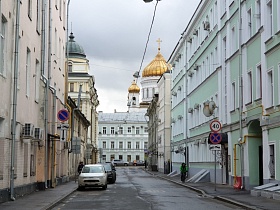 вид церкви с золотыми куполами за трехэтажным домом на краю небольшой улицы Лебяжий переулок между жилыми домами в историческом центре Москвы