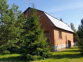 кирпичный двухэтажный дачный домик с высоким цоколем из камня на участке с небольшими елями и высокими соснами в Годуново