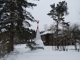 монумент с пятиконечной красной звездой во дворе старинной деревянной школы в зимнее время