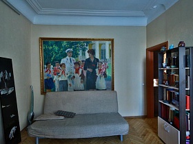 большая картина с изображением Гагарина и Терешковой  с детьми в пионерском лагере над мягким серым диваном и серый книжный шкаф в светлой гостиной стильной квартиры художника