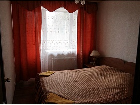 настольная лампа на тумбочке у аккуратно заправленной кровати в номере с красными шторами