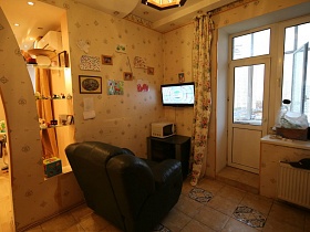 мягкое черное кресло у стены с детскими рисунками и телевизором в углу у балконной двери современной трешки