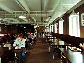 общий вид уютного зала столовой бизнес центра с белым потолком, коричневыми стенами и рядами столов со стульями на полу с квадратной плиткой