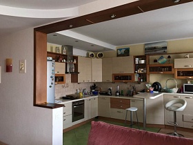двухцветная бежево коричневая кухня со встроенной газовой плитой, металлической вытяжкой, посудой на открытых полках, барными стульями у барной стойки современной квартиры бухгалтера