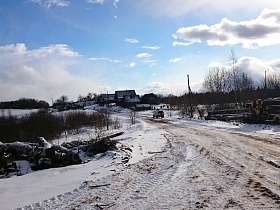 машина на проселочной дороге заброшенной деревни со старыми деревянными домами и грудами бревен на снегу