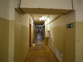 указатель лестничного перехода на желтых стенах длинного коридора с комнатами в комунальном общежитии