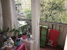 упакованные вещи в клетчатое зеленое покрывало и красную скатерть  у окрашенных досок открытого балкона двухкомнатной квартиры в Останкино
