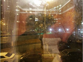 вид из окна через гардину на соседние жилые дома и дорогу с припаркованными машинами
