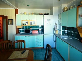 многочисленные кувшины, вазы, чайники на поверхности голубой кухни в зонированной комнате квартиры оператора