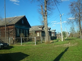 дорога, поросшая зеленой травой на одной из улиц старой российской деревни с рядами деревянных бревенчатых домов