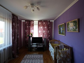 детская деревянная кроватка у фиолетовой стены с большими цветочными картинами в яркой спальне семейной уютной дачи с видом на город