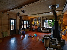 круглый серый камин в центре гостиной, фотографии под стеклом в рамках на деревянной стене над пианино, канапе у большого окна уютного загородного дома