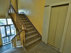 желтые стены чистого ухоженного подъезда с большими окнами и лестницей с перилами между этажами с лифтом в сталинке