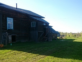 жилой деревянный дом с голубыми нальчниками на окнах, деревянной лестницей с перилами и открытой дверцей в подполе