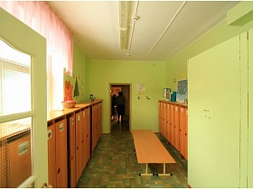 детские шкафчики и банкетка в зеленой раздевалке группы детского сада