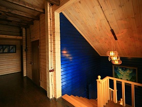 вид с прихожей в мансарде на ярко синие стены лестничных маршей деревянного загородного дома из восьми комнат