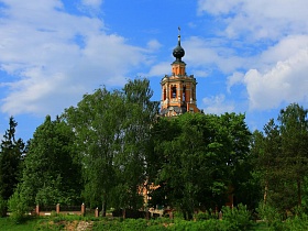 стройна высокая церковь со звездами на небольшом темном куполе на восьмигранной колокольне под ярким синим небом в живописном месте Подмосковья