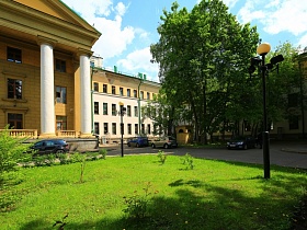 подстриженная зеленая трава на газоне с кустарниками, цветами и фонарным столбом с желтым плафоном на территории усадьбы СССР