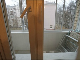 раскладушка у стены застекленного балкона сквозь окно гостиной съемной трехкомнатной квартиры с ресепшн