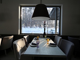 большой темный абажур подвесного светильника над деревянным сервированным столом с мягкими креслами у окна с кальяном на подоконнике, с видом на лес