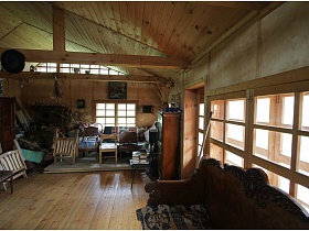 многочисленные деревянные стулья, диван, шкафы в комнате с балками под потолком деревянного домика на дачном участке