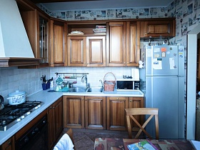 серый холодильник у коричневой стенки с многочиленными шкафчиками, полками в кухне семейной трешки