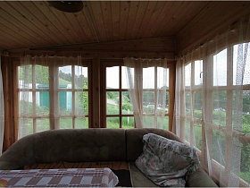 мягкий угловой диван у окон деревянной дачи с прозрачной белой гардиной