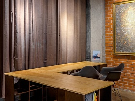 коричневые кресла, угловой большой деревянный стол с книгами на открытых полках в ножках у окна с коричневыми шторами в студии лофт в серых тонах