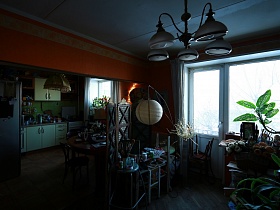серый холодильник, белая кухня и круглый обеденный стол из мастерской через открытый дверной проем трехкомнатной квартиры времен СССР
