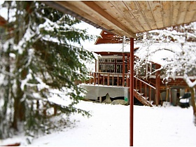 снег на крыше открытой террасы с лестницей и перилами соседней бревенчатой дачи на участке со снегом