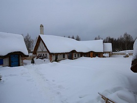невысокие елочки у домиков с цветными ставнями на окнах на территории ресторана , стилизованного под хутор в коттеджном поселке зимой