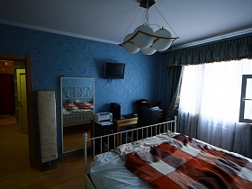 большое зеркало, телевизор на стене, принтер и столик с креслом в углу голубой спальной комнаты трехкомнатной актерской квартиры