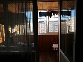 белье на веревке и кресло на застекленном деревянном балконе через открытую дверь спальной комнаты трешки в многоэтажном жилом доме